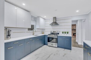 A modern kitchen with blue cabinets, a stainless steel range, and a marble floor. - Modern Home w. Large Dining Area | Playset & WiFi (Suffern)