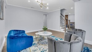 Un salon moderne avec un fauteuil bleu, des canapés gris, une table basse ronde et un lustre.