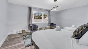 Une chambre d’hôtel avec un grand lit, deux fauteuils, une petite table et une fenêtre donnant sur un beau paysage.