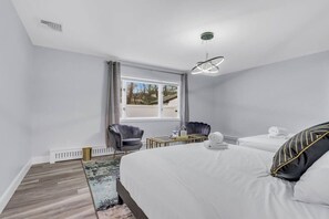 A hotel room with a large bed, two armchairs, a small table, and a window with a view. - Modern Home w. Large Dining Area | Playset & WiFi (Suffern)