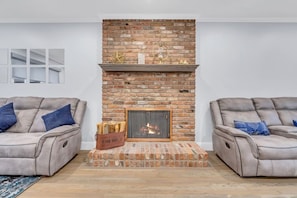 A living room with a brick fireplace, two leather sofas, and a small rug.