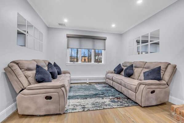 A room with two beige sofas, a patterned rug, and a window with blinds.
