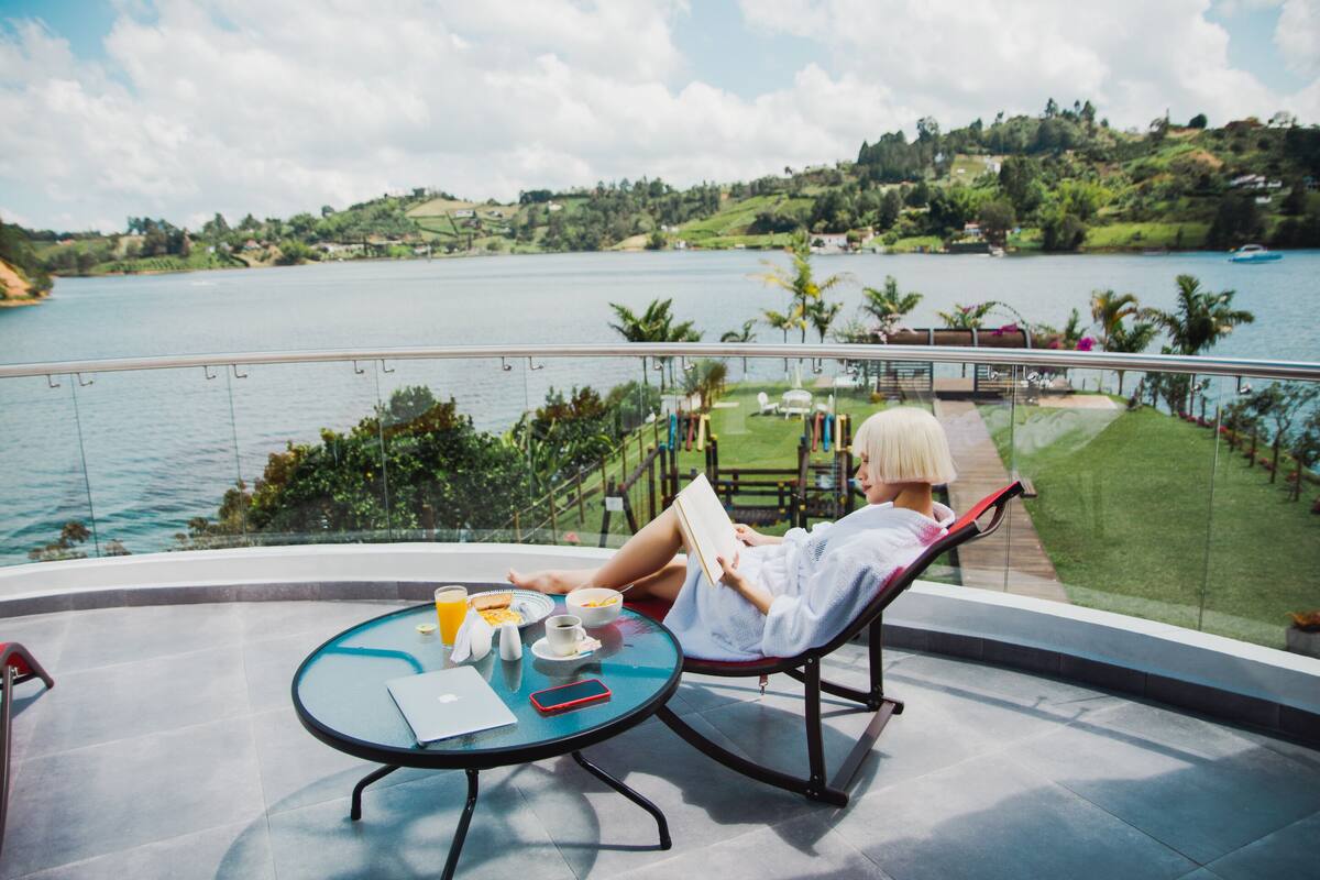 A person relaxing on a balcony with a view of a lake and greenery.