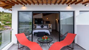 Un balcón con una cama, una mesa adornada con flores y dos sillas rojas.