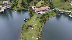 An aerial view of a large house with a red roof, surrounded by a well-maintained lawn and a small dock. - Jordan Hotel Boutique (El Peñol)