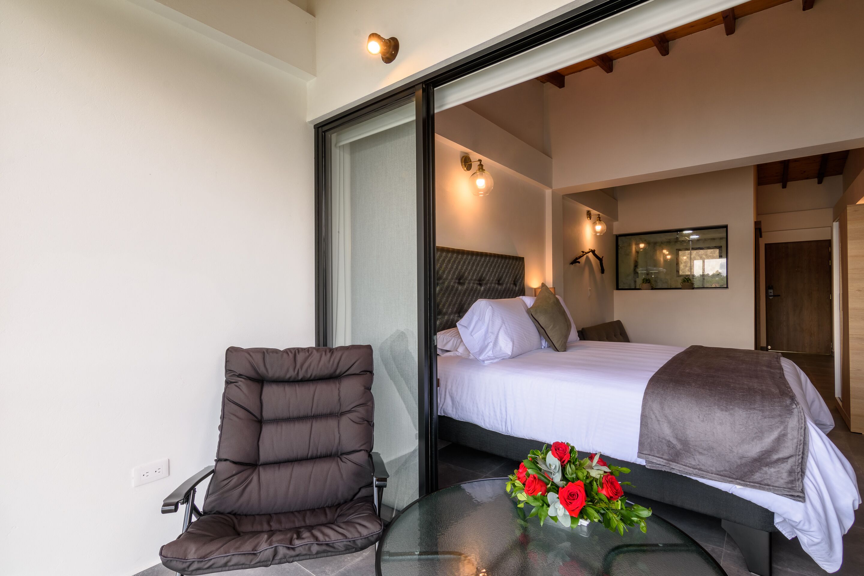 Un dormitorio moderno con una cama, una silla y una mesa de vidrio con un arreglo floral.