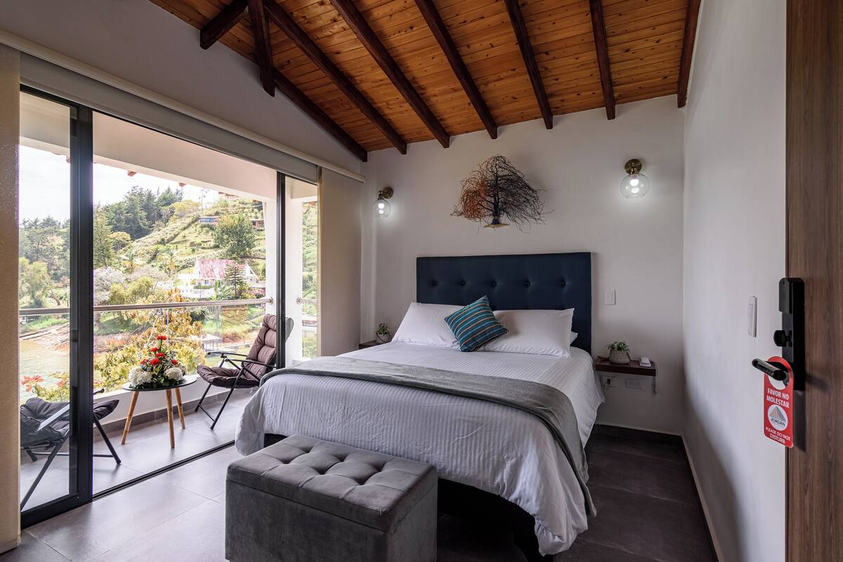 A bedroom with a large bed, a view of the outdoors, a balcony, and a wooden ceiling.