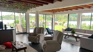 A spacious living room with a large window offering a view of a lake and greenery. There are multiple seating options including sofas and armchairs. - Jordan Hotel Boutique (El Peñol)