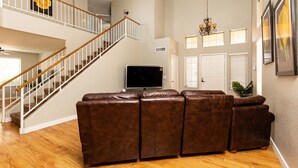 A spacious living room with a brown leather sectional sofa, a flat-screen TV, a staircase, and a chandelier. - Walk to Stadium|Westgate|Glendale (Glendale)