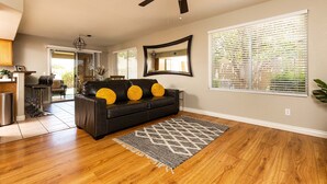 A living room with a black leather sofa, wooden flooring, a ceiling fan, and a large window with blinds. - Walk to Stadium|Westgate|Glendale (Glendale)