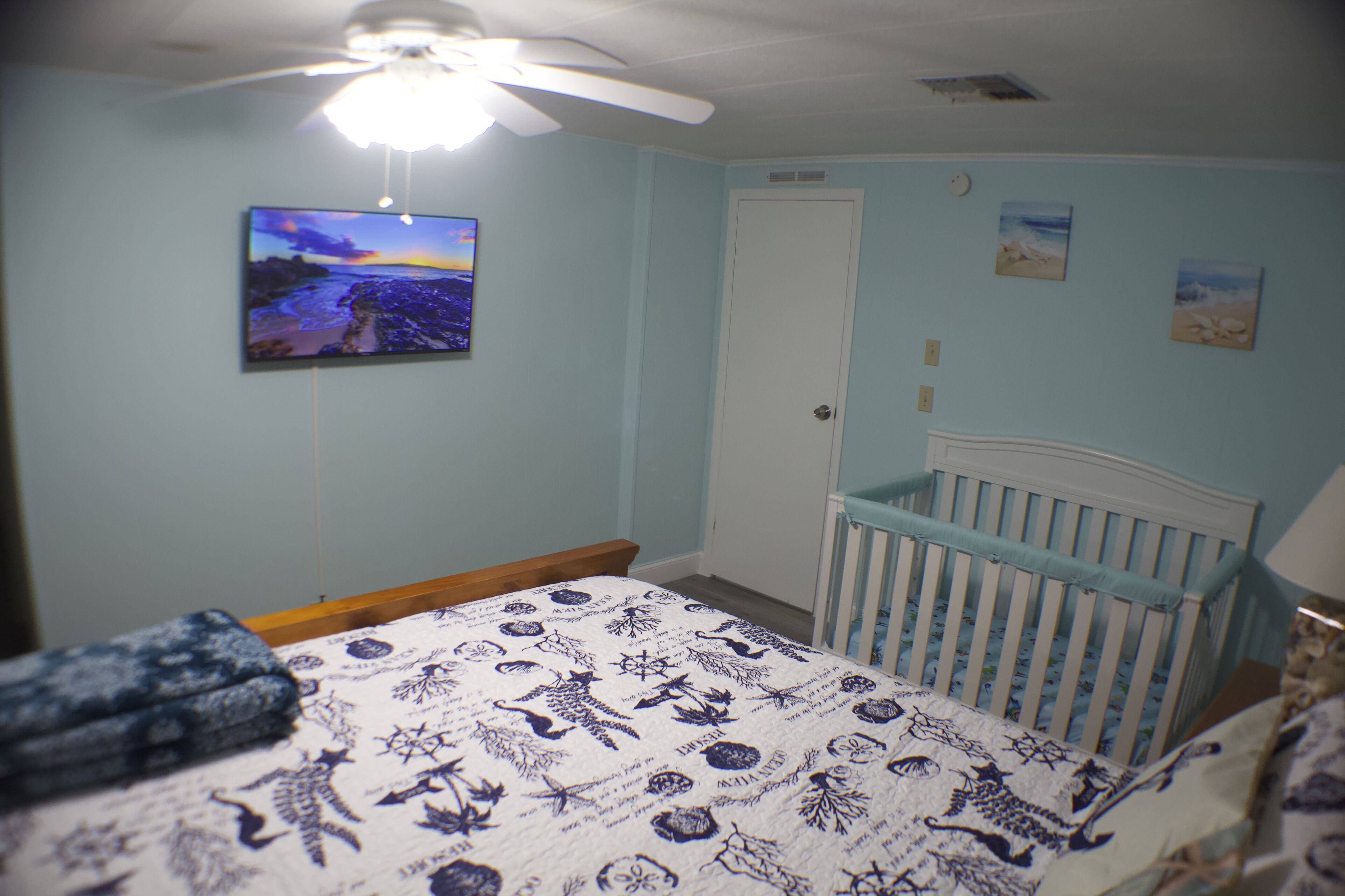 Un dormitorio con una cama, una cuna, un ventilador de techo y un televisor montado en la pared.