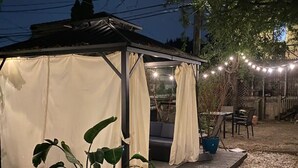 Ein überdachter Außenbereich mit einer Pergola, Lichterketten und Blumentöpfen.