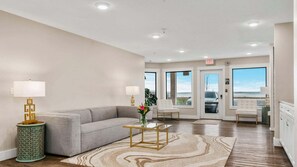 A hotel lobby with a grey sofa, two lamps, a glass coffee table, and a patterned rug.