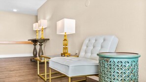 A hotel room with a tufted armchair, a side table with a lamp, and a decorative metal planter. - 🏖️ Gold Coast Inn | Breathtaking Sunsets w/ Lake View ➠ 102 (Traverse City)