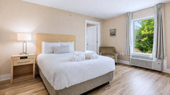Ein Hotelzimmer mit Bett, Nachttisch, Sessel und einem Fenster mit Blick auf Grünflächen.