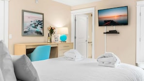 A hotel room with a bed, a desk, a chair, a TV, and a door.