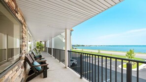 A covered outdoor area with a view of a body of water, a parking lot, and a row of chairs.