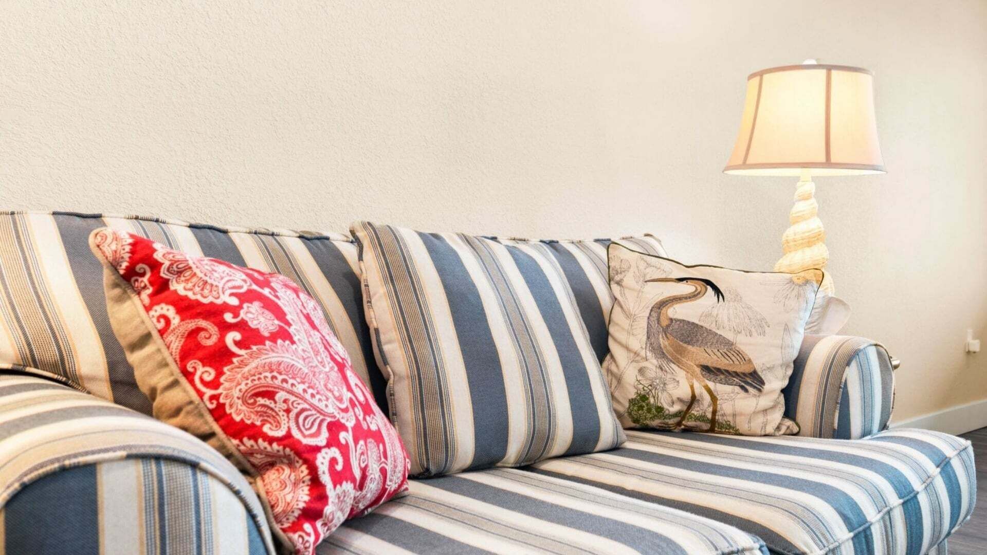 A striped sofa with decorative pillows and a table lamp.