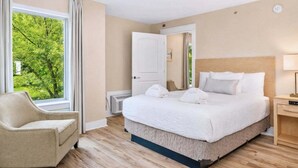 Een hotelkamer met een bed, een stoel, een nachtkastje en een raam met uitzicht op groen.