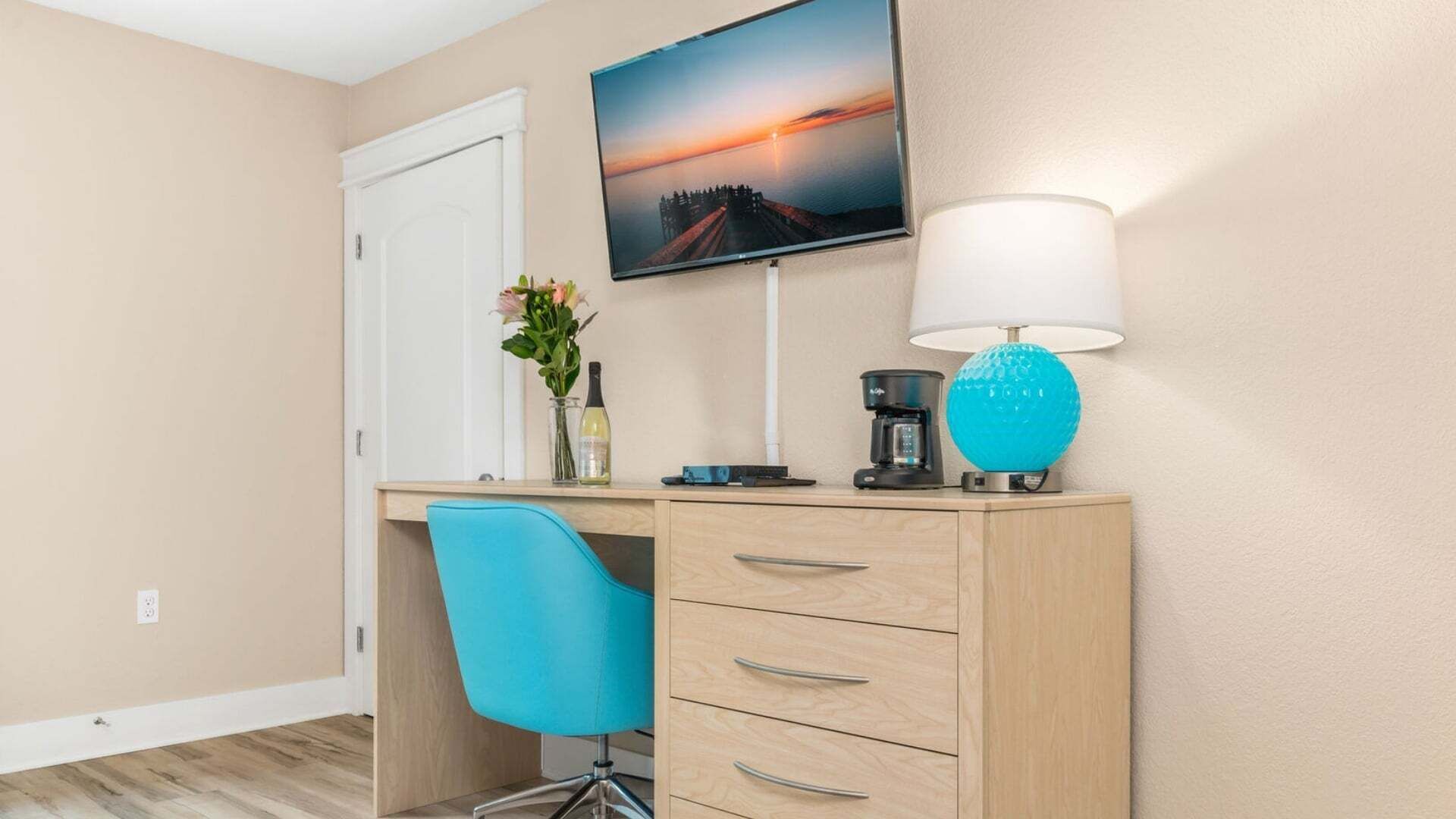 Une chambre d’hôtel équipée d’un bureau, d’une chaise, d’un téléviseur fixé au mur et d’une lampe.