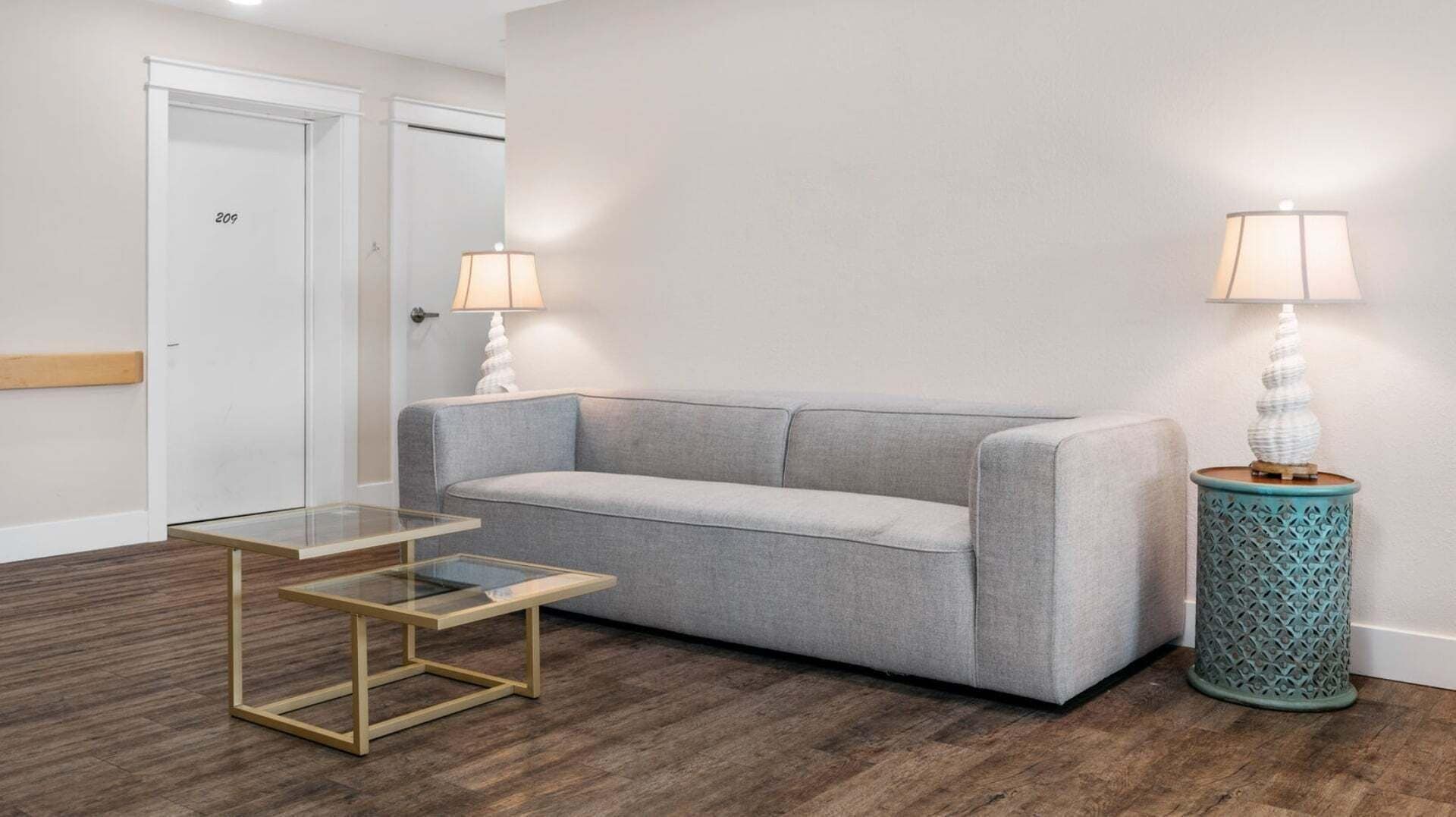 Gray sofa between table lamps with a gold-framed glass coffee table in front.