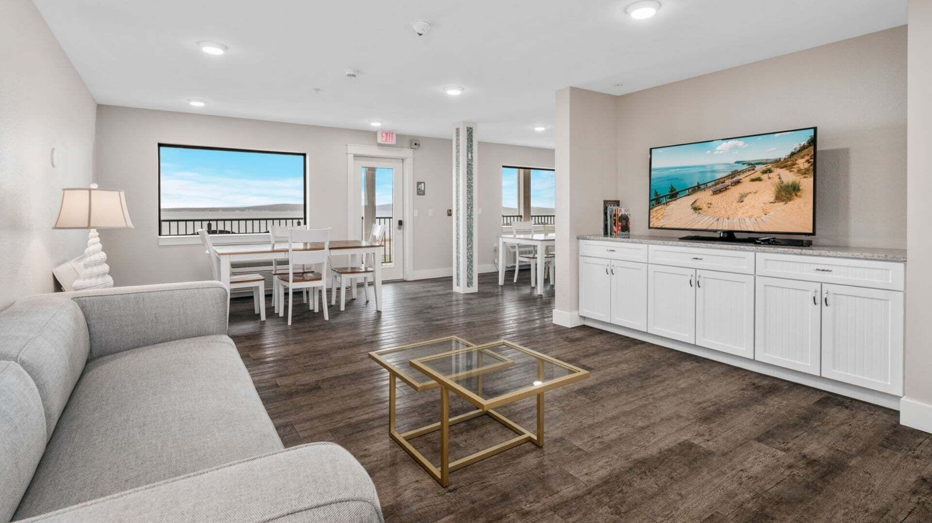 Gray sofa and glass coffee table in a shared lounge with television, white cabinets and bay-view windows.