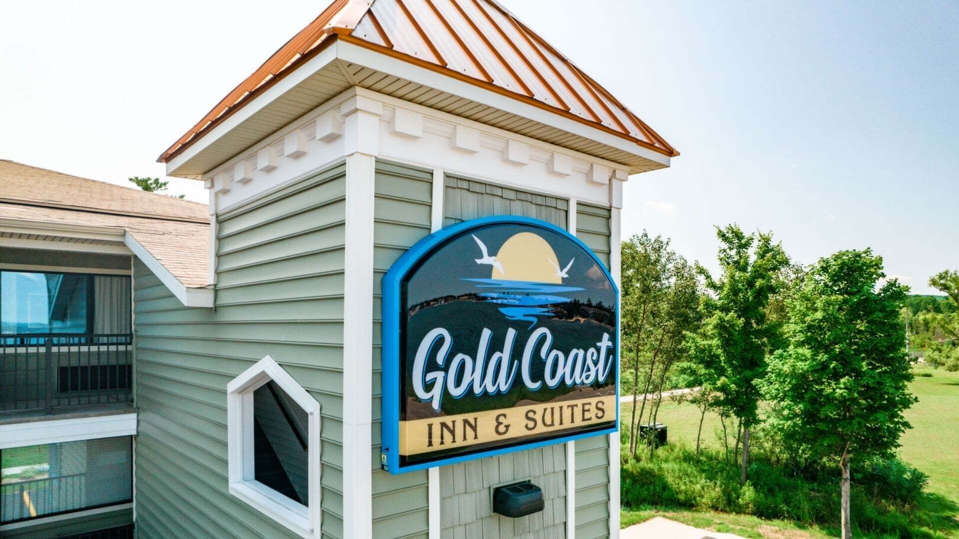 Een gebouw met een bord waarop 'Gold Coast Inn & Suites' staat, met een zonsondergang en meeuwen.