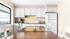 Una cocina moderna con armarios blancos, una mesa de comedor de madera y un refrigerador.