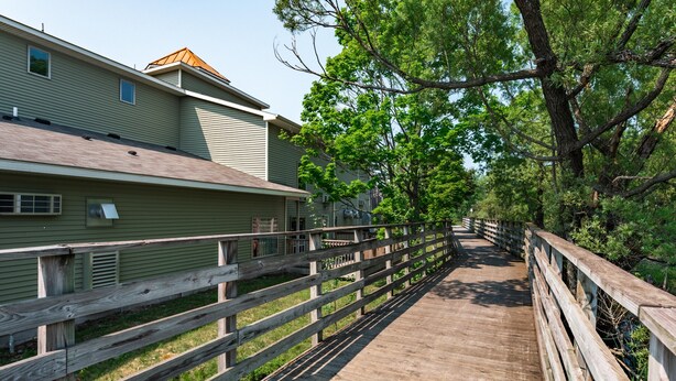 A wooden boardwalk leading to a building with a sloped roof and a small window. - 🏖️ Gold Coast Inn | Breathtaking Lake Views • Corner Rm 108 (Traverse City)