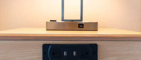 A wooden surface with a black electrical outlet and a metal object above it.