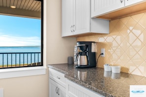 A kitchen with a coffee maker, two cups, and a view of the sea.