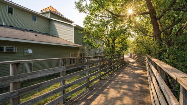 A wooden boardwalk leading to a building with a green exterior and a sloped roof.
