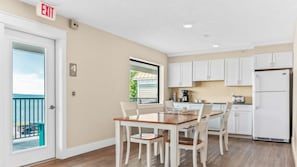 A kitchen with white cabinets, a dining table with chairs, and a view of the outside. - 🏖️ Gold Coast Inn | Breathtaking Lake Views • Corner Rm 201 (Traverse City)