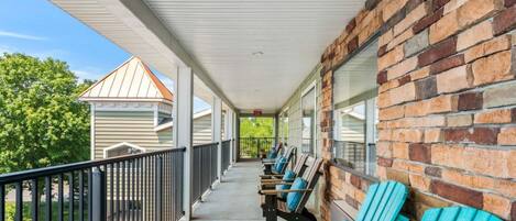 En overdækket veranda med murstensvæg, gelænder og flere Adirondack-stole.