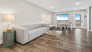 Una sala de estar moderna con un sofá, una mesa de centro y lámparas. Hay un comedor con sillas y una mesa, y una puerta que da al exterior.