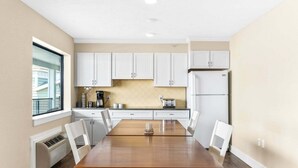 A modern kitchen with white cabinets, a wooden dining table, and a built-in oven. - 🏖️ Gold Coast Inn | Breathtaking Sunsets w/ Lake View ➠ 106 (Traverse City)