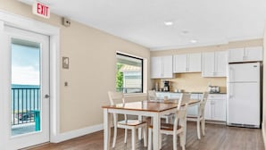 A kitchen with white cabinets, a dining table with chairs, and a view of the outside. - 🏖️ Gold Coast Inn | Breathtaking Sunsets w/ Lake View ➠ 202 (Traverse City)