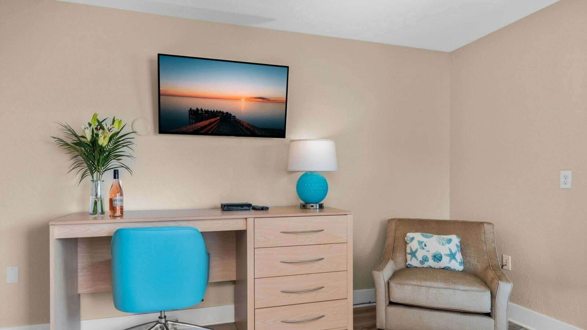 A hotel room with a desk, chair, and a wall-mounted lamp.