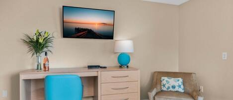 A hotel room with a desk, chair, and a wall-mounted lamp.