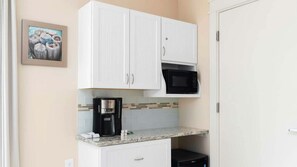 Een kleine keuken met witte kasten, een koffiezetapparaat, een magnetron en een betegelde spatwand.