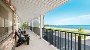 Ein überdachter Balkon mit Sitzgelegenheit im Freien, Blick auf eine Straße und ein Gewässer sowie einen klaren Himmel.