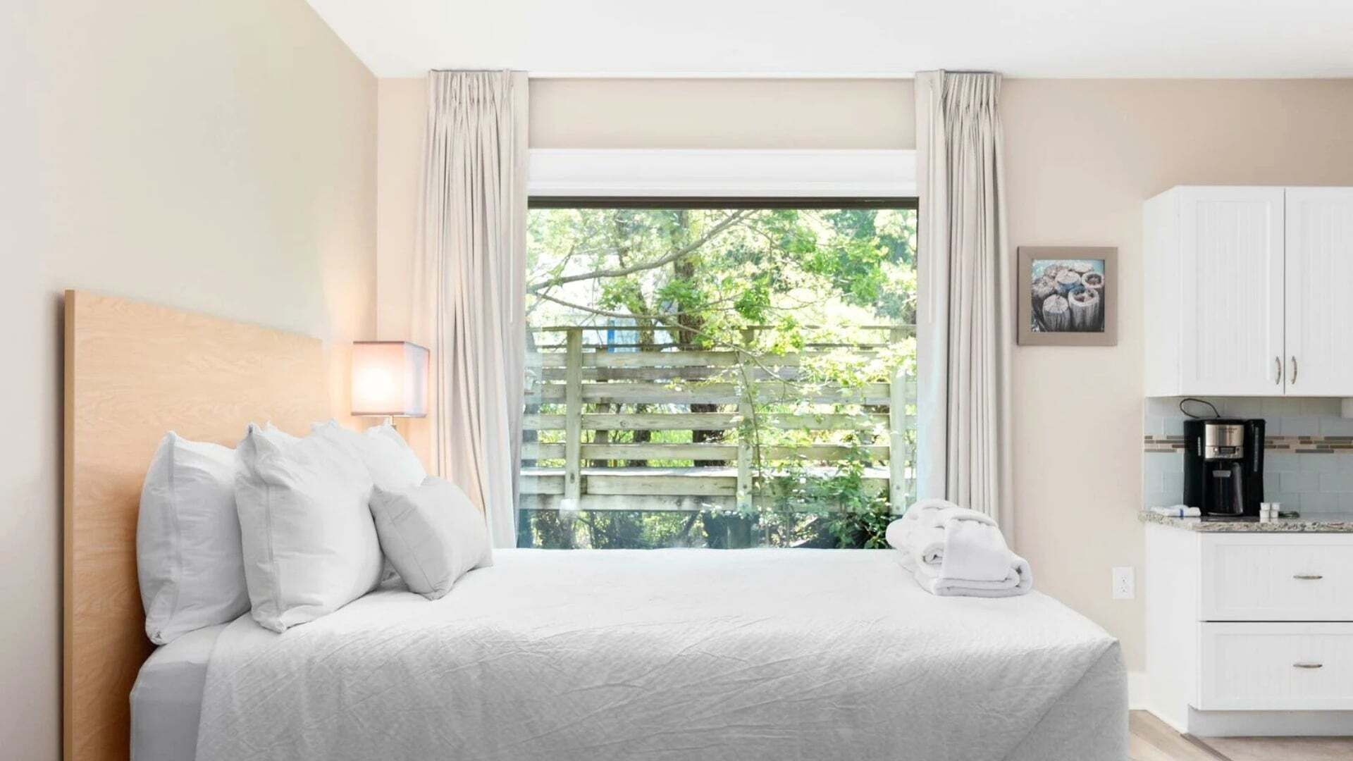 Une chambre d’hôtel avec un lit, une fenêtre avec des rideaux, une table de chevet, une lampe, une machine à café et une vue sur la verdure.