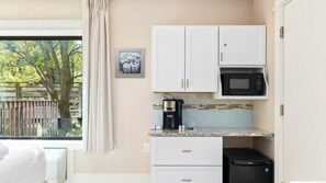 A compact kitchen with white cabinets, a microwave, a coffee maker, and a trash bin.
