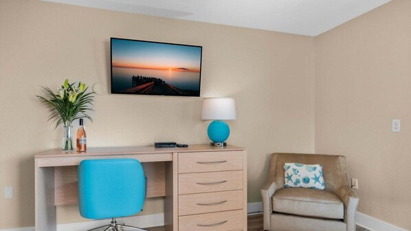 A hotel room with a desk, chair, and a wall-mounted lamp.