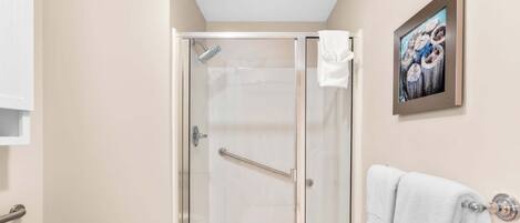 A glass-enclosed shower with a handrail, a white towel hanging on the wall, and a framed picture above the towel.