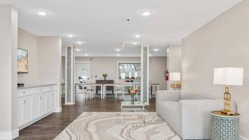 A modern living room with a sofa, a coffee table, and a lamp. There is a kitchen area with cabinets and a dining table.