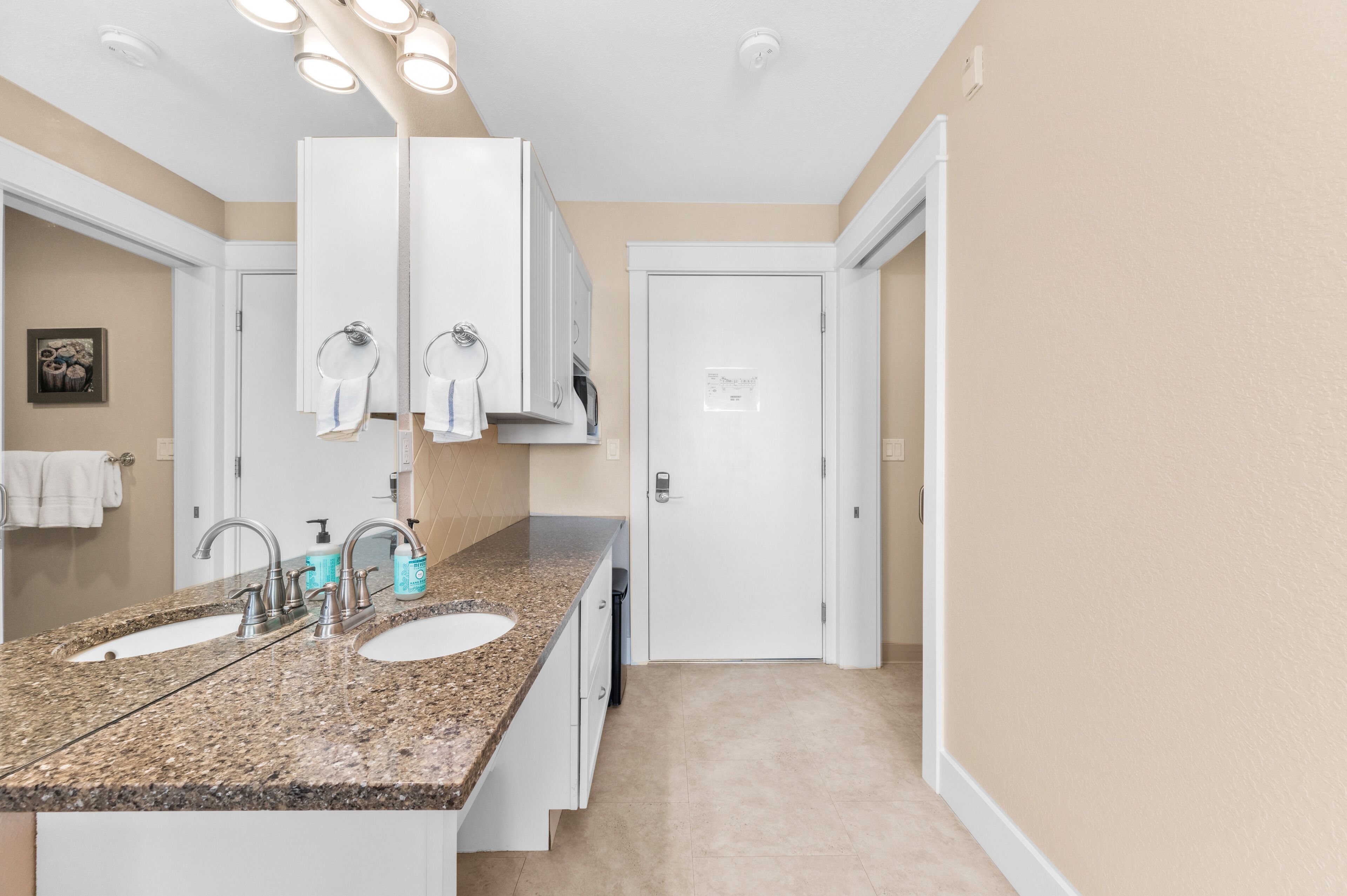 Granite vanity with sink, mirror and white cabinets beside the bathroom doorway.