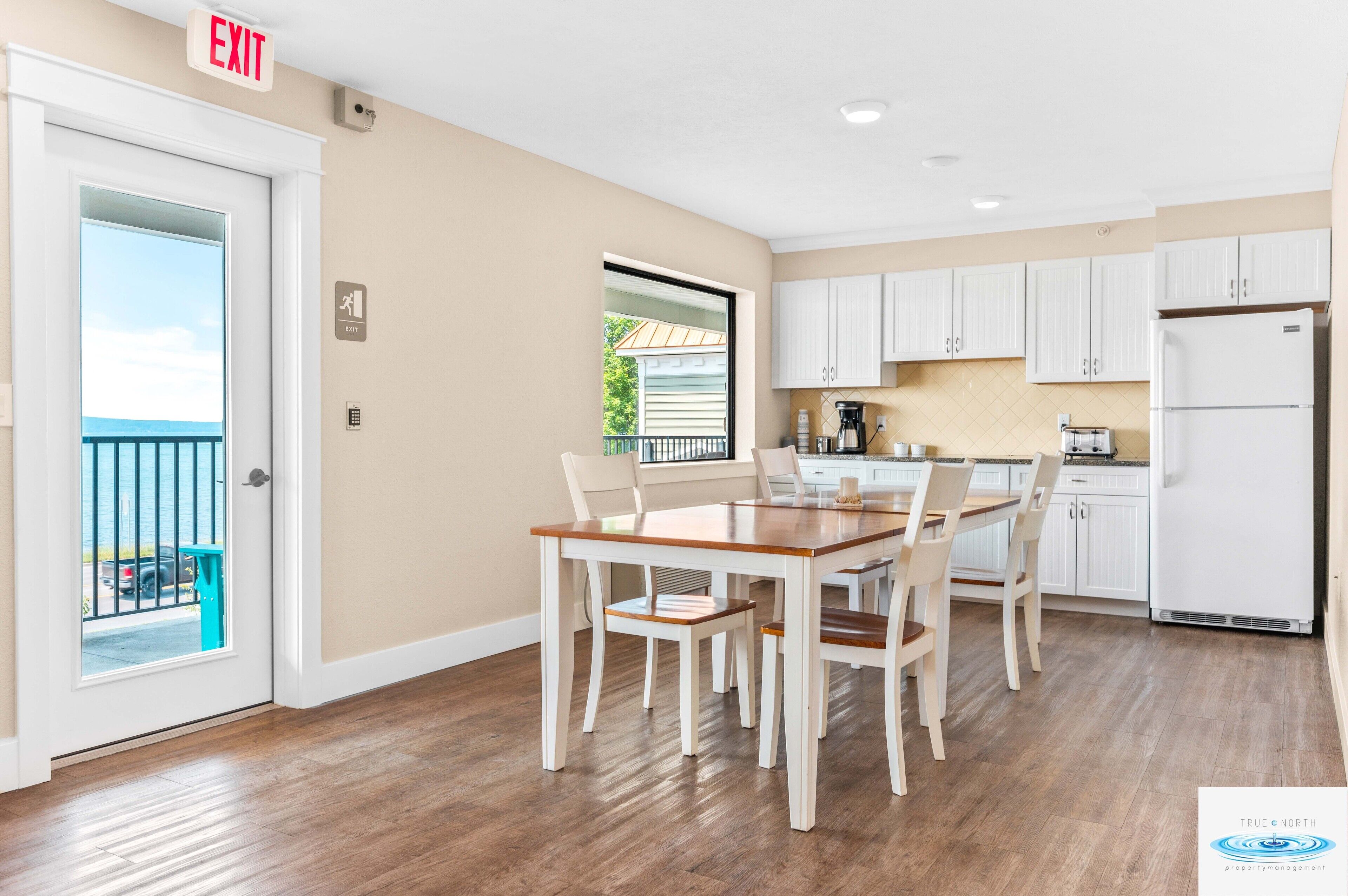 A kitchen with white cabinets, a wooden dining table, and a view of a balcony.