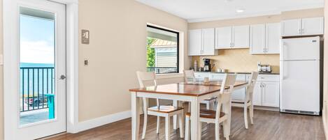 A kitchen with white cabinets, a wooden dining table, and a view of a balcony.