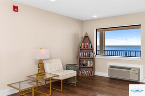 Una habitación con un sofá blanco, una mesa de vidrio, una estantería y vista al mar.